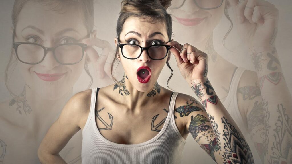 Tätowierte Frau mit Brille und überraschtem Gesichtsausdruck, Symbolbild zum Thema Kosten eines Cover-up-Tattoos