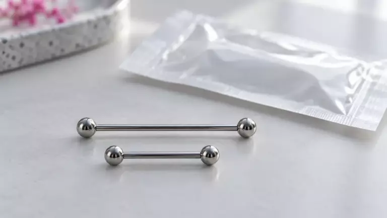 Zwei Titan-Piercingstäbe in lang und kurz neben einer Sterilverpackung (Symbolbild)